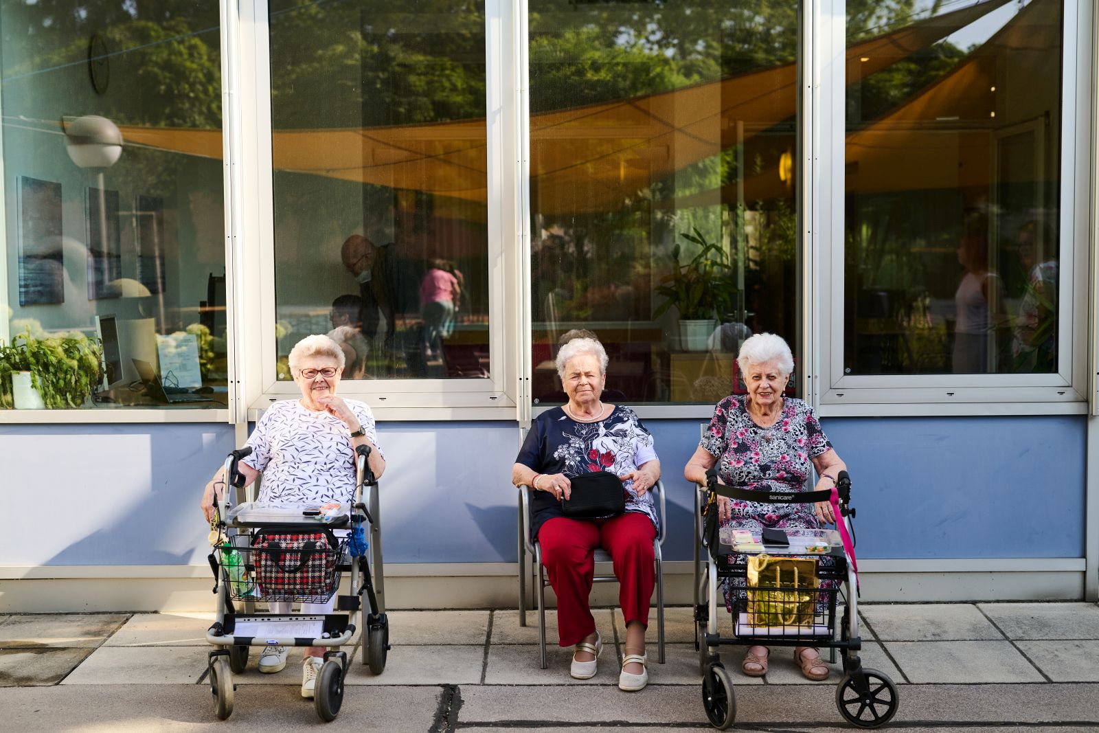 Seniorinnen mit Rollatoren sitzen vor einem Haus
