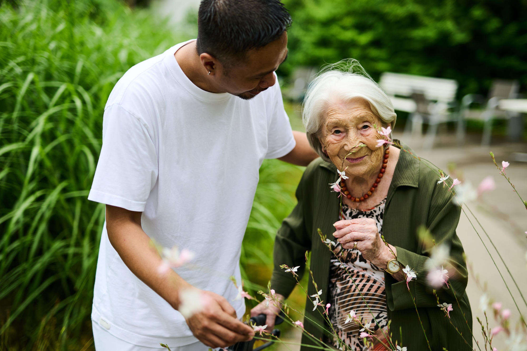 Ein Pfleger ist mit einer älteren Dame in einem Garten