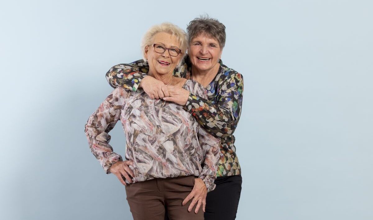 Zwei Seniorinnen umarmen sich und lachen.