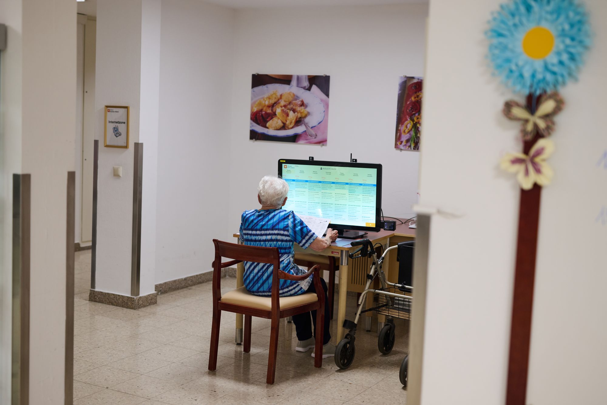 Eine Seniorin von hinten sitzt an einem Computer, an dem sie Essen bestellt.
