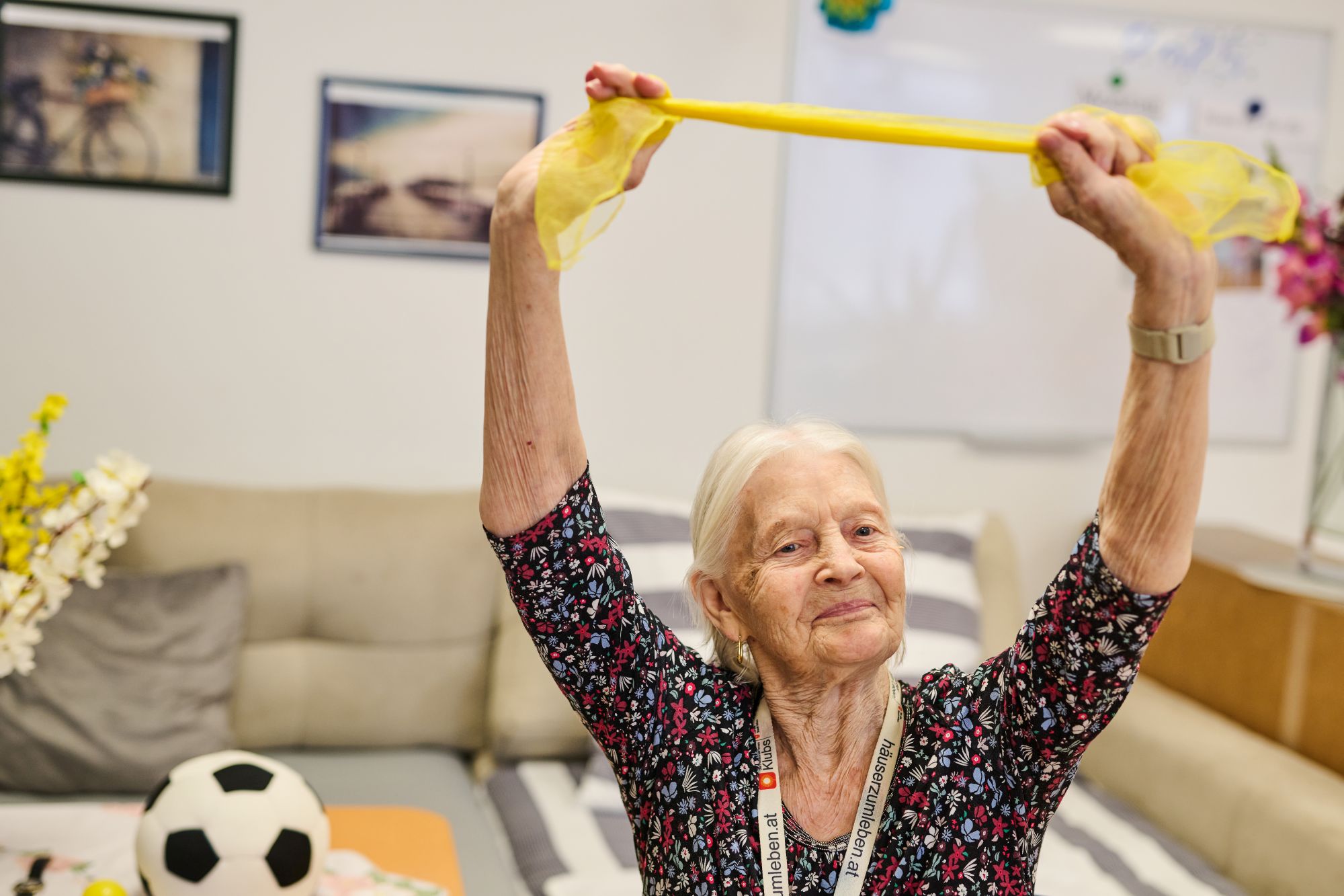 Eine Seniorin streckt ein Theraband mit beiden Armen nach oben.