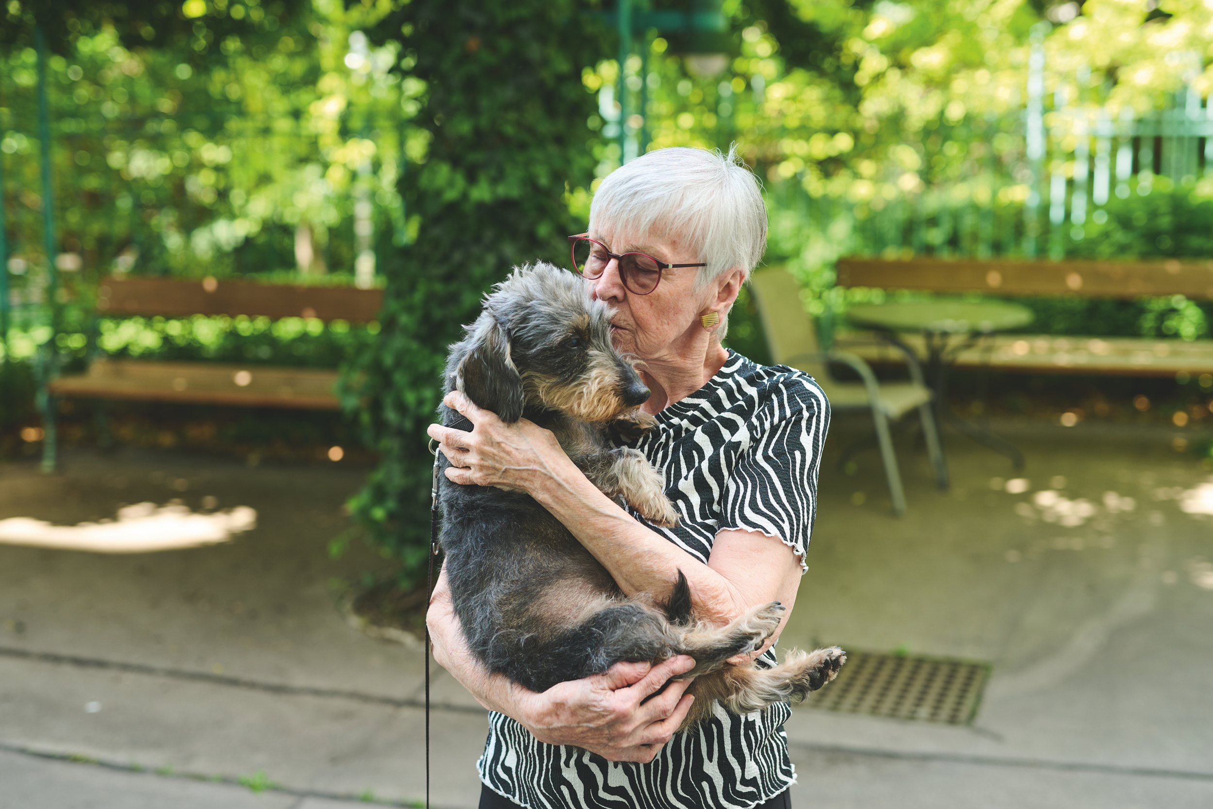 Eine Frau mit kurzen grauen Haaren und Brille hält einen Hund.